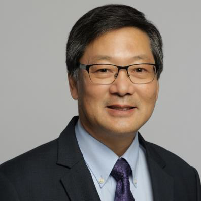 A headshot of Gary Yamaguchi PhD wearing a dark suit with a light button-up shirt and sark purple tie.